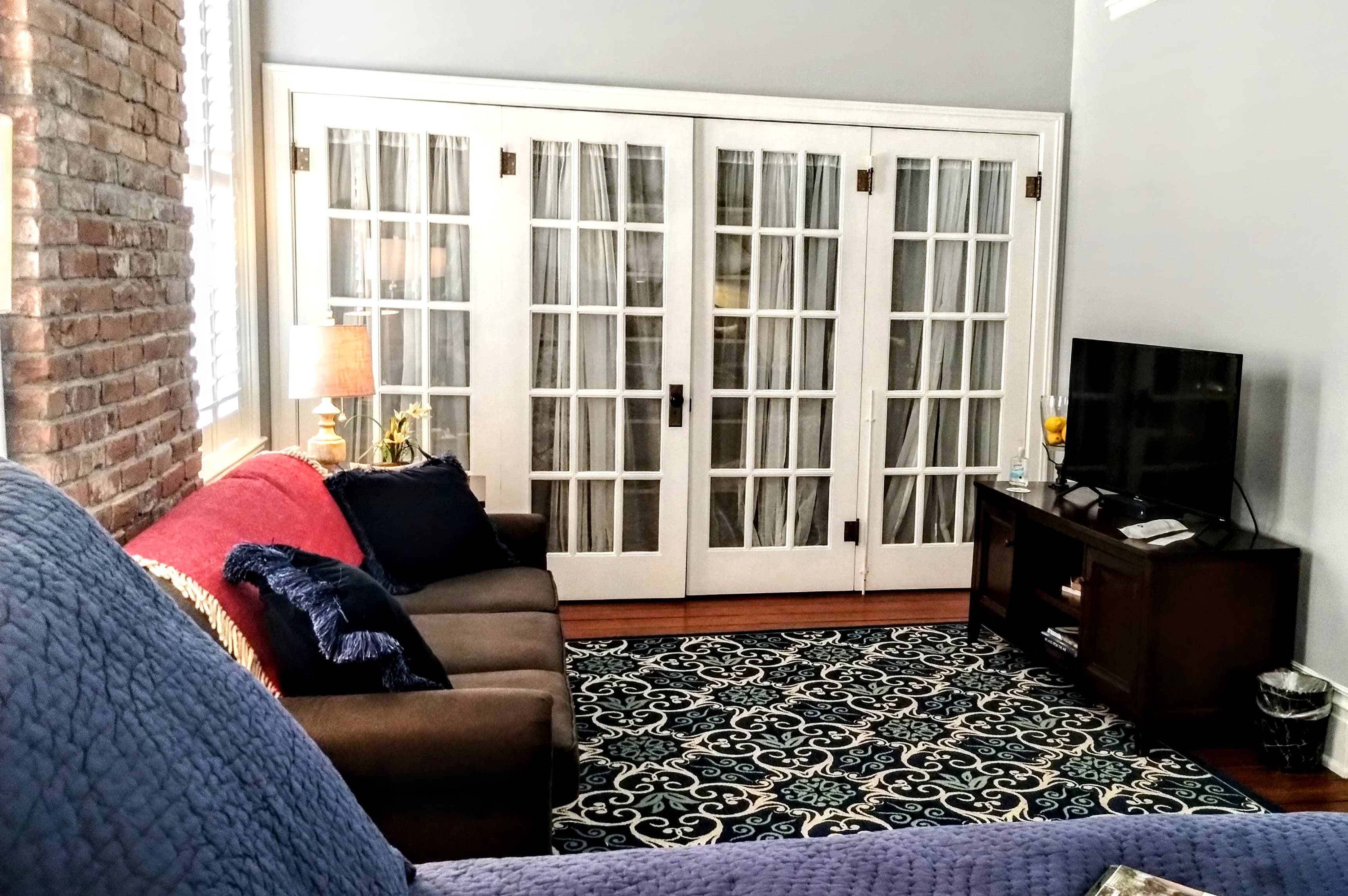 A sitting area with a brown leather couch, a patterned rug, and white sliding glass doors.
