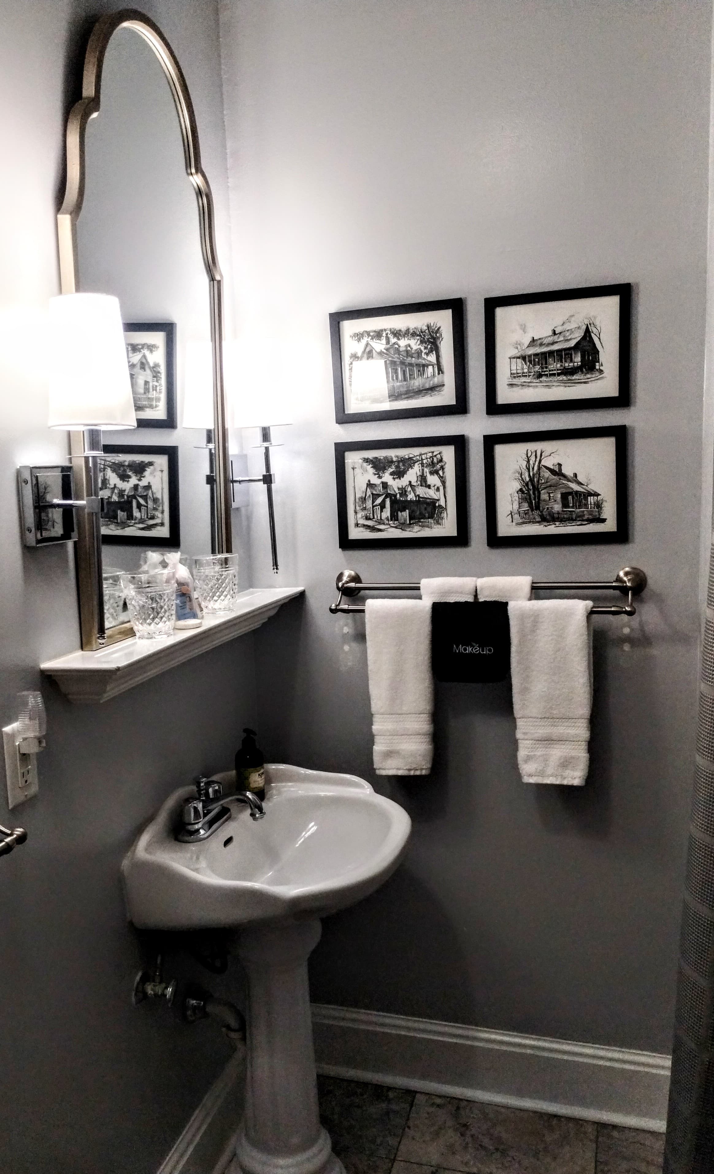 A bathroom with a white pedestal sink, a curved mirror, and framed black and white photos.