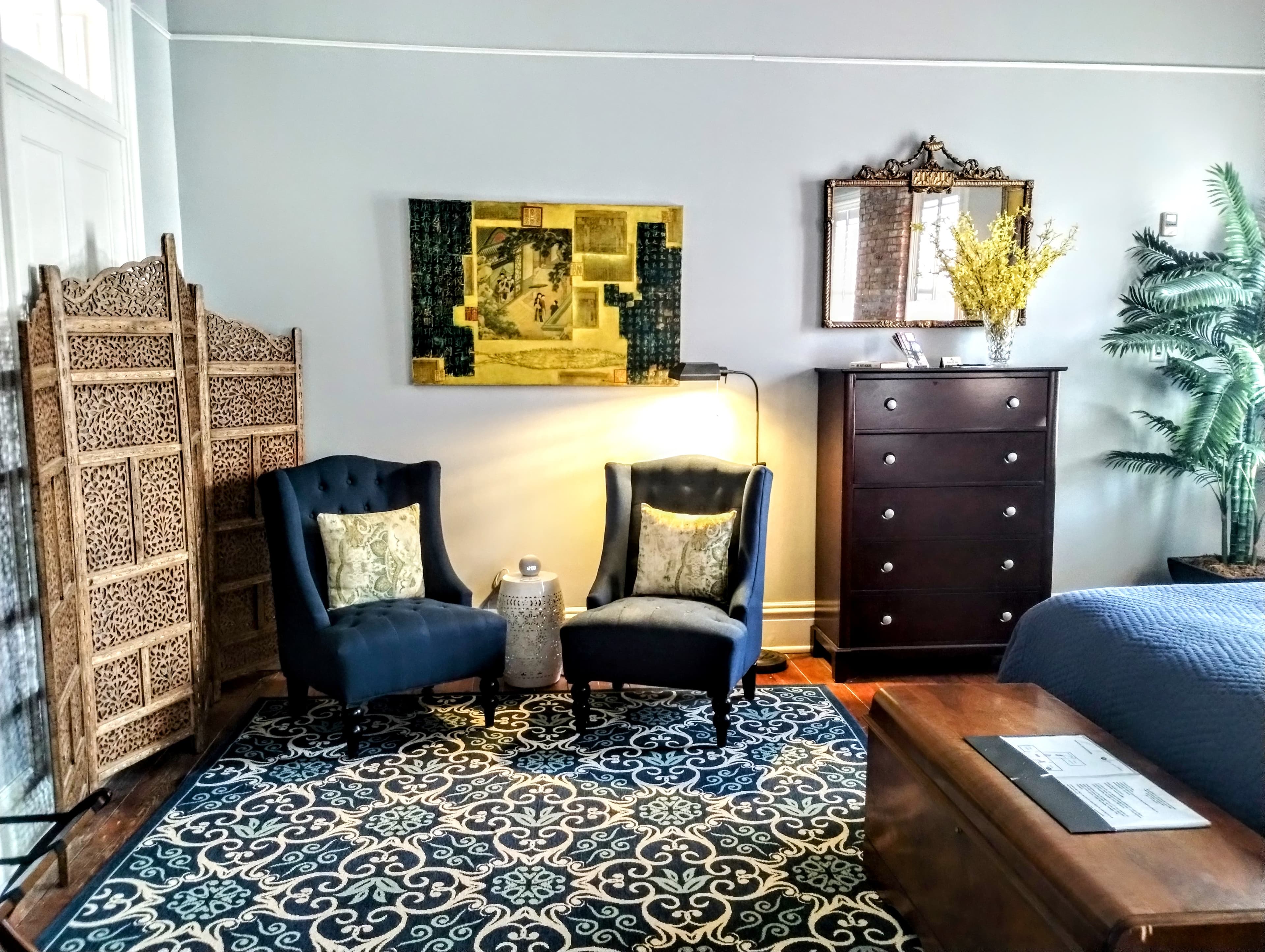 A cozy corner with two blue armchairs, a wooden dresser, a patterned rug, and artwork.