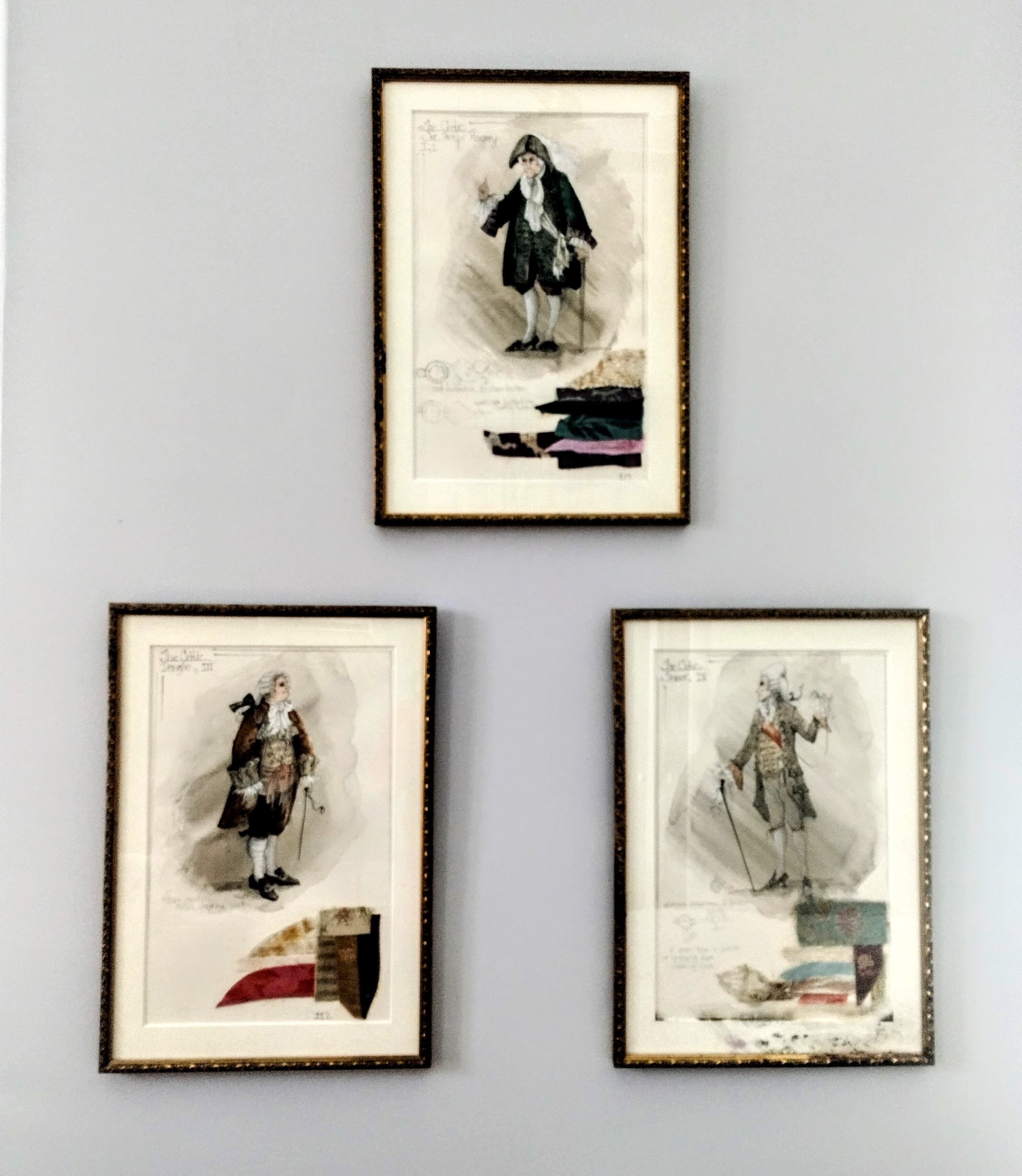 Three framed drawings of men in historical clothing, arranged in a triangular pattern on a light gray wall.