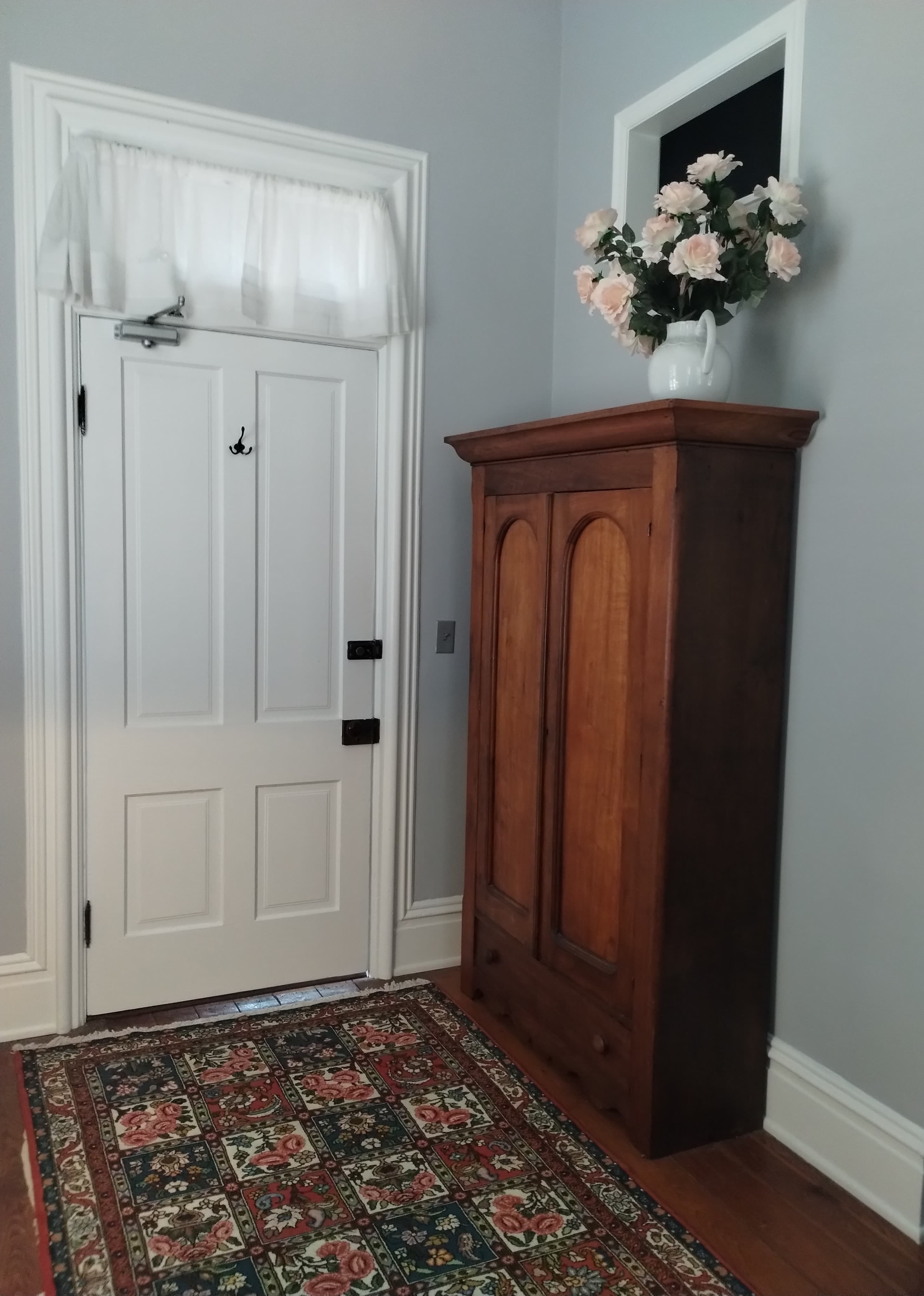 A white door with a sheer curtain, a wooden cabinet with flowers, and a patterned rug.