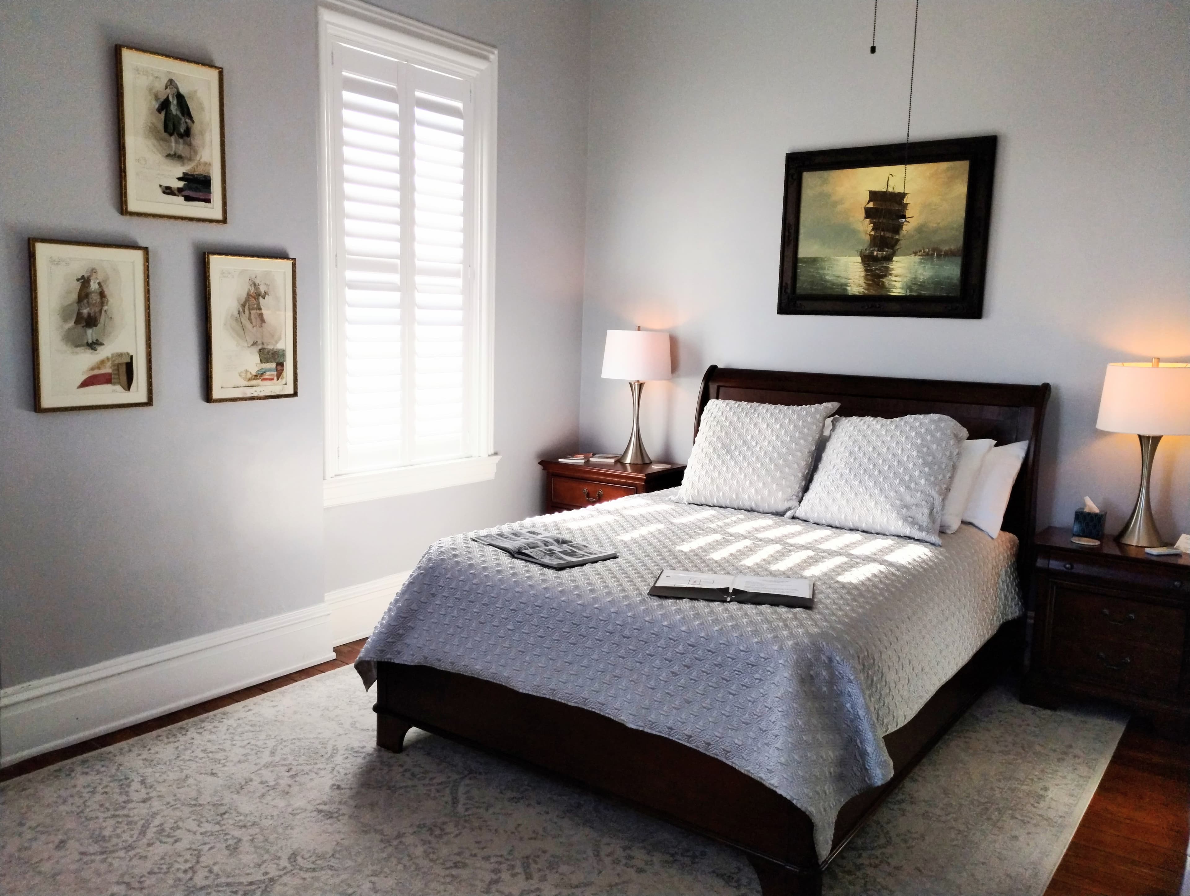 A tranquil bedroom with a dark wood bed, white linens, framed pictures on the wall, and two bedside lamps.