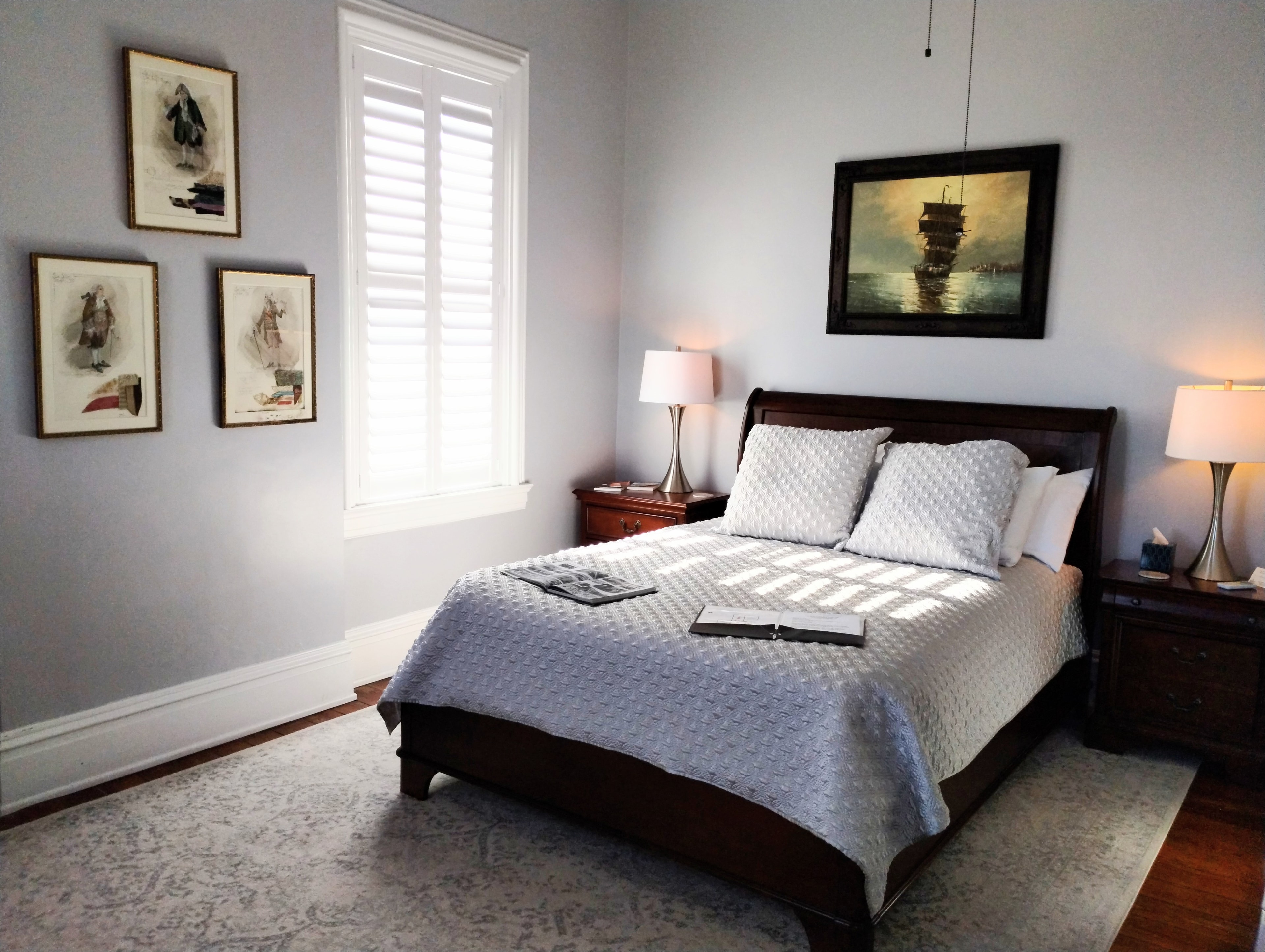 A tranquil bedroom with a dark wood bed, white linens, framed pictures on the wall, and two bedside lamps.