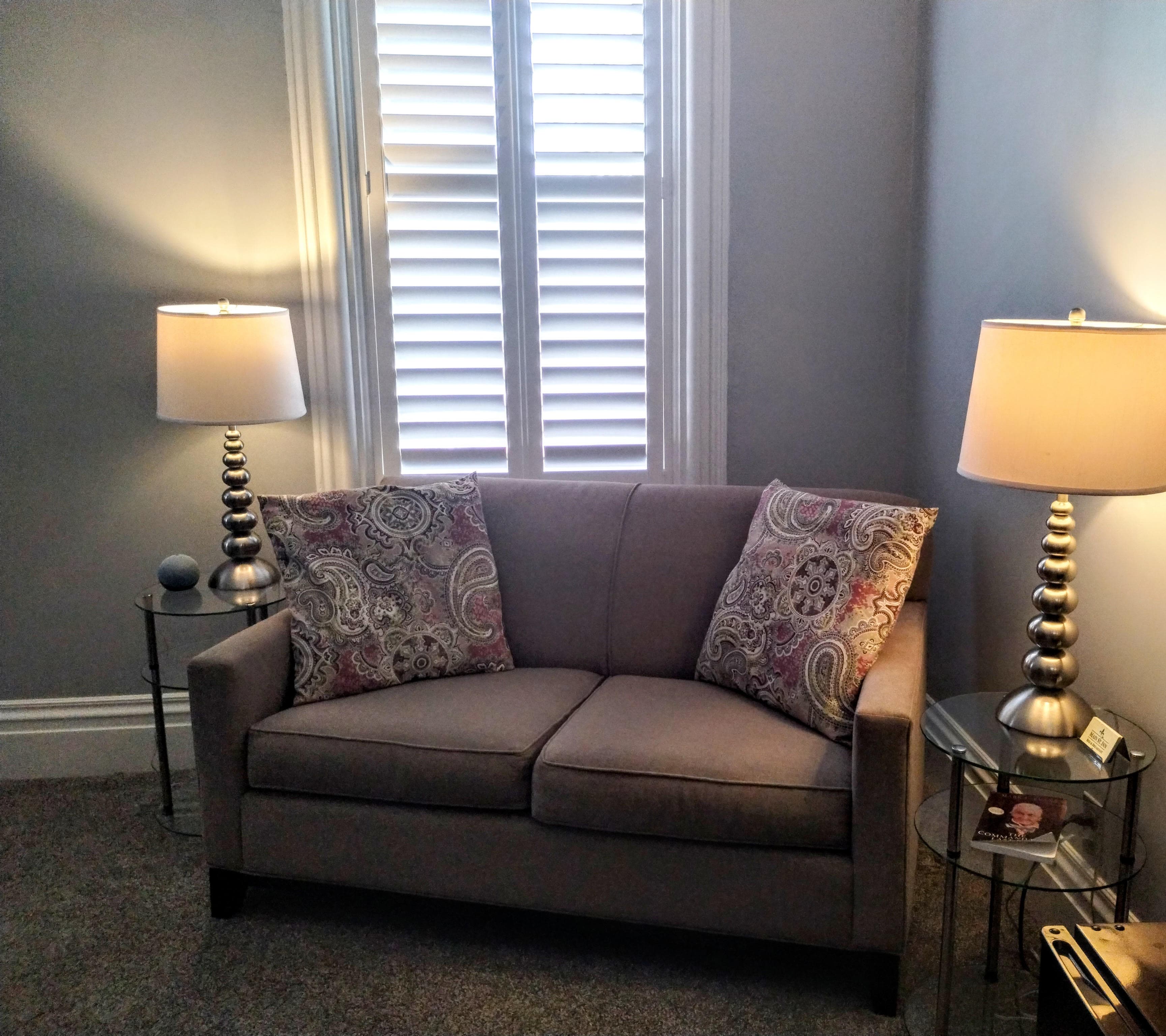 A small gray couch with patterned pillows, flanked by two lamps on side tables.