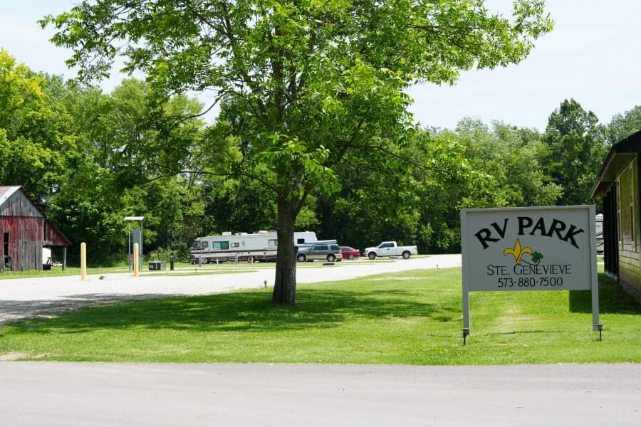 A sign for an RV park surrounded by trees and parked vehicles.