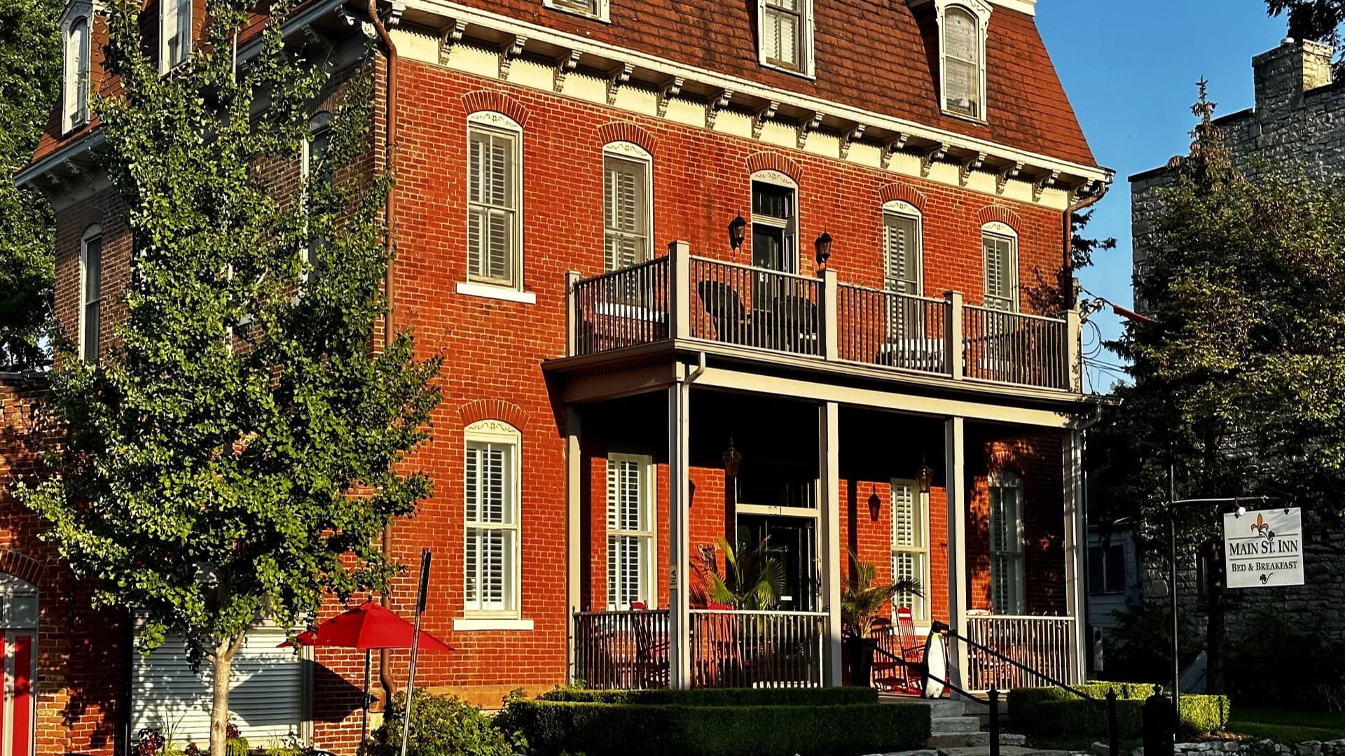 Historic two-story brick inn with a front porch and lush greenery.