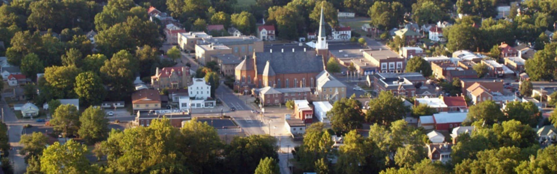 Aerial view of a small town with a mix of residential and commercial buildings surrounded by trees.