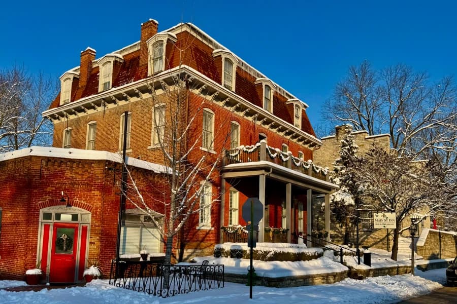 A historic brick house with a snowy landscape and clear blue sky.