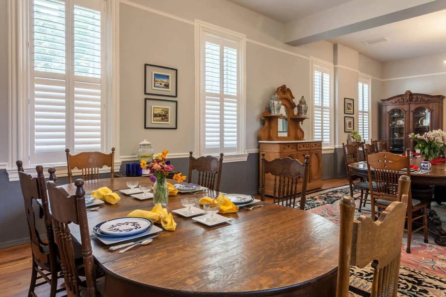 A cozy dining room features a wooden table set with plates, glasses, and yellow napkins, surrounded by chairs and elegant decor.
