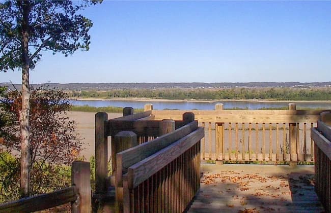 View of a river from a wooden observation deck surrounded by trees.