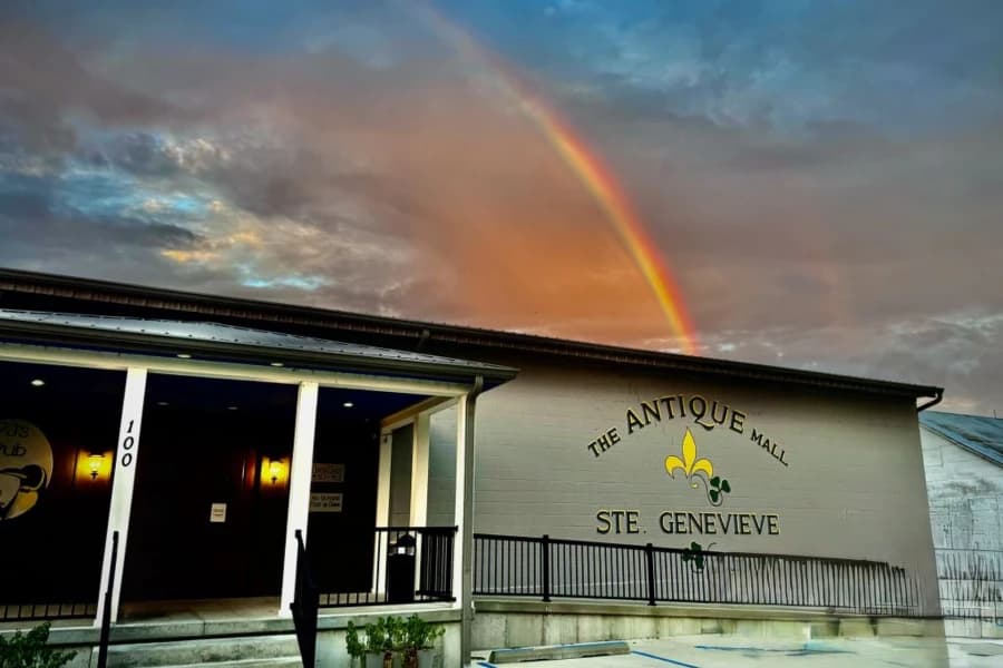 A quaint antique mall in Ste. Genevieve under a colorful rainbow and dramatic sky.