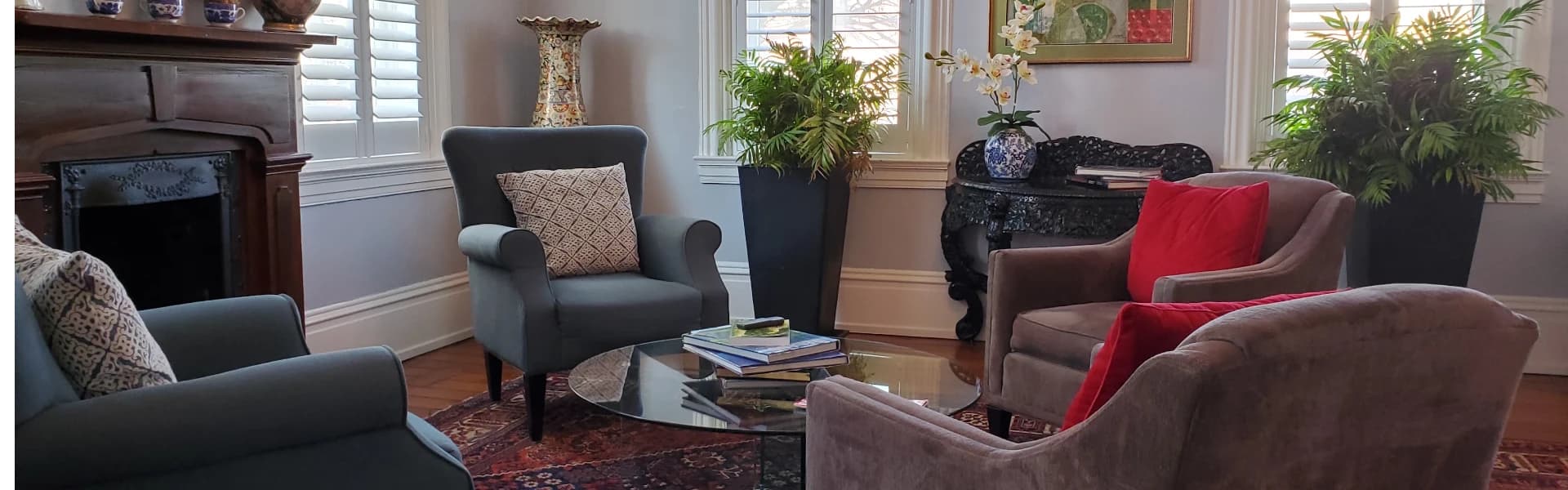 A cozy living room featuring two armchairs, a glass coffee table, and large houseplants.